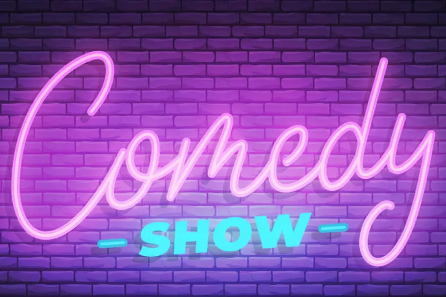 Pink neon Comedy Show sign on a brick wall